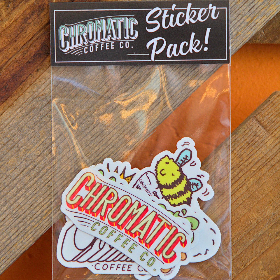 A sticker pack from Chromatic Coffee Co. displayed on a wooden surface, including various stickers with coffee-related illustrations and text.