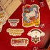 A collection of colorful stickers with unicorn and castle illustrations, branding for Chromatic Coffee, and other related designs laid out on a red surface.